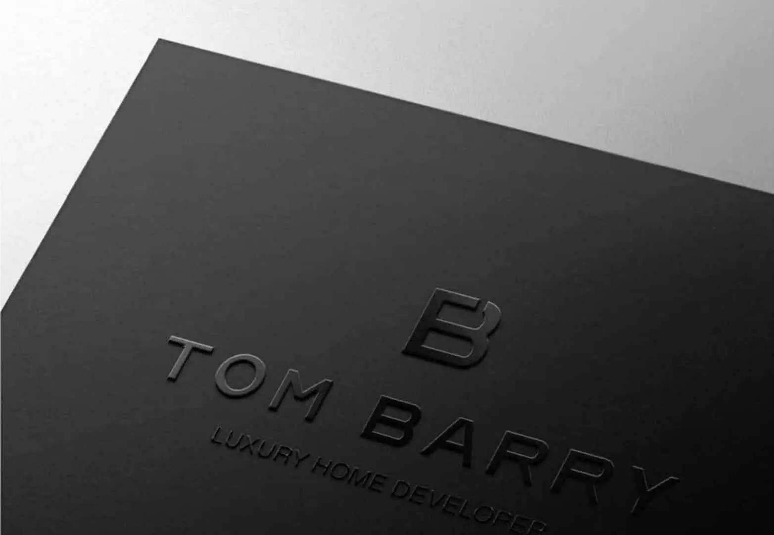 Cartão de visita preto da TOM Barry com o monograma em relevo seco.